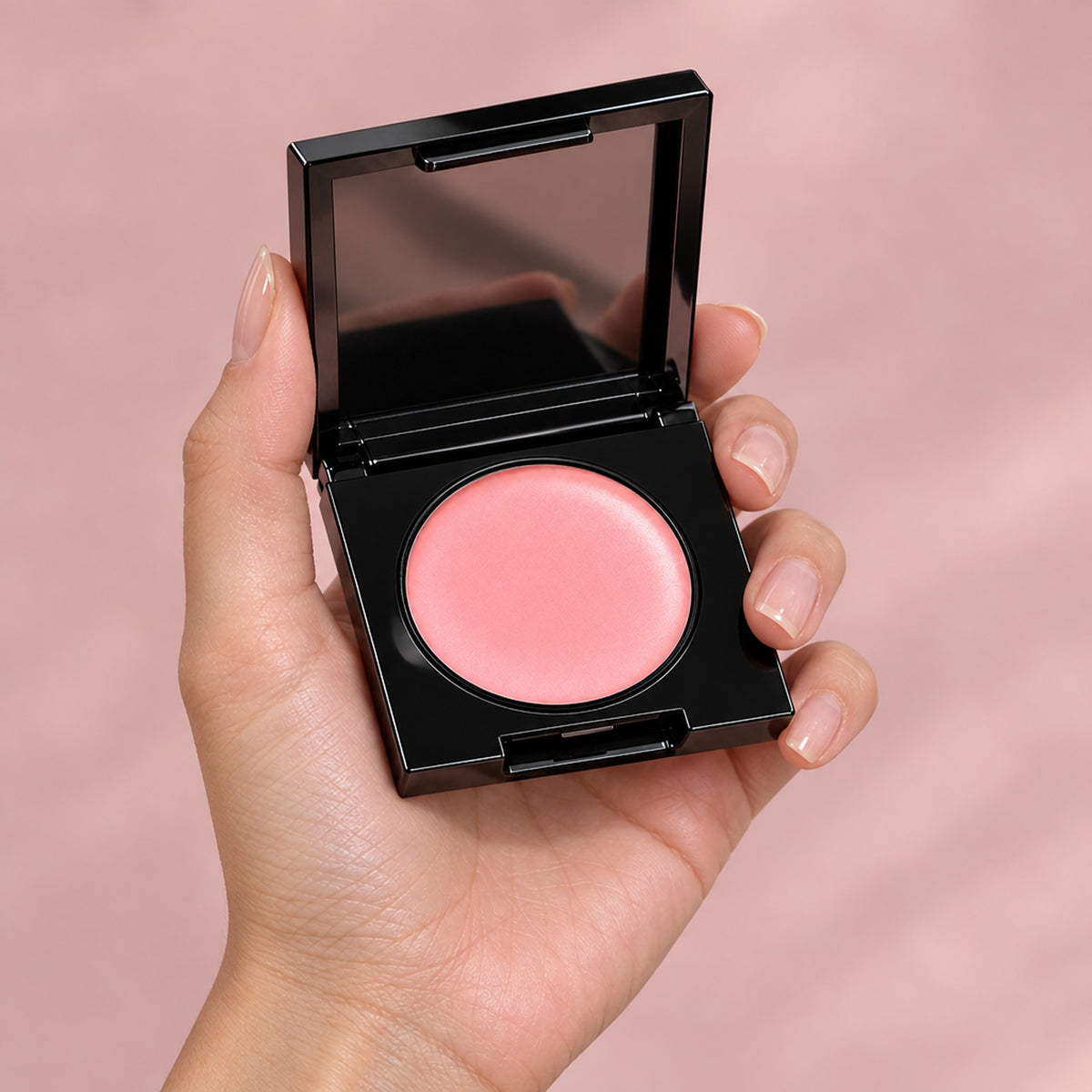 Hand håller öppen kompakt med rosa concealerkräm